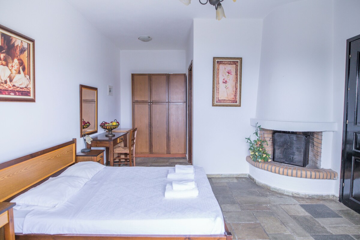 A bedroom with a bed, a desk, a chair, a wardrobe, and a fireplace.