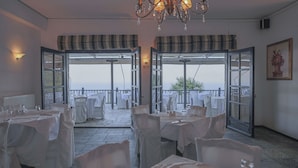 Un restaurante con mesas preparadas para comer, una araña y vistas a través de puertas abiertas.
