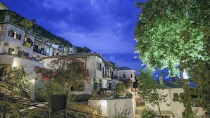 Un pueblo en la ladera con edificios blancos, balcones y un árbol en primer plano.