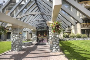 A hotel entrance with a stone pillar, a glass canopy, and a well-maintained lawn.