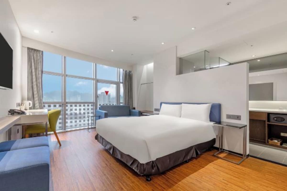 Habitación de hotel moderna con una cama grande, un escritorio, una silla y vistas a la ciudad.