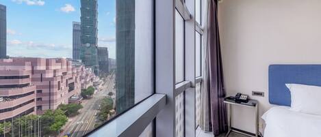 A hotel room with a view of a cityscape, including a tall building and a busy street.