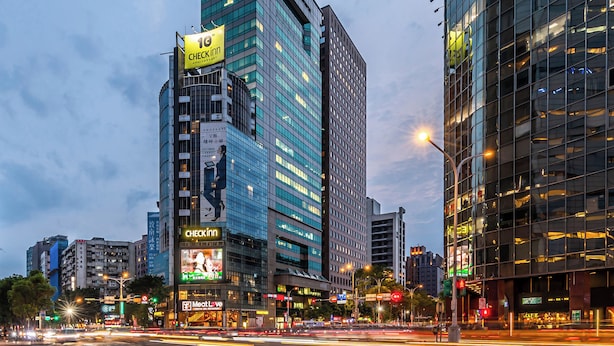 Un hotel urbano moderno con un llamativo letrero de Checkinn, una terraza en la azotea y vistas a la ciudad.
