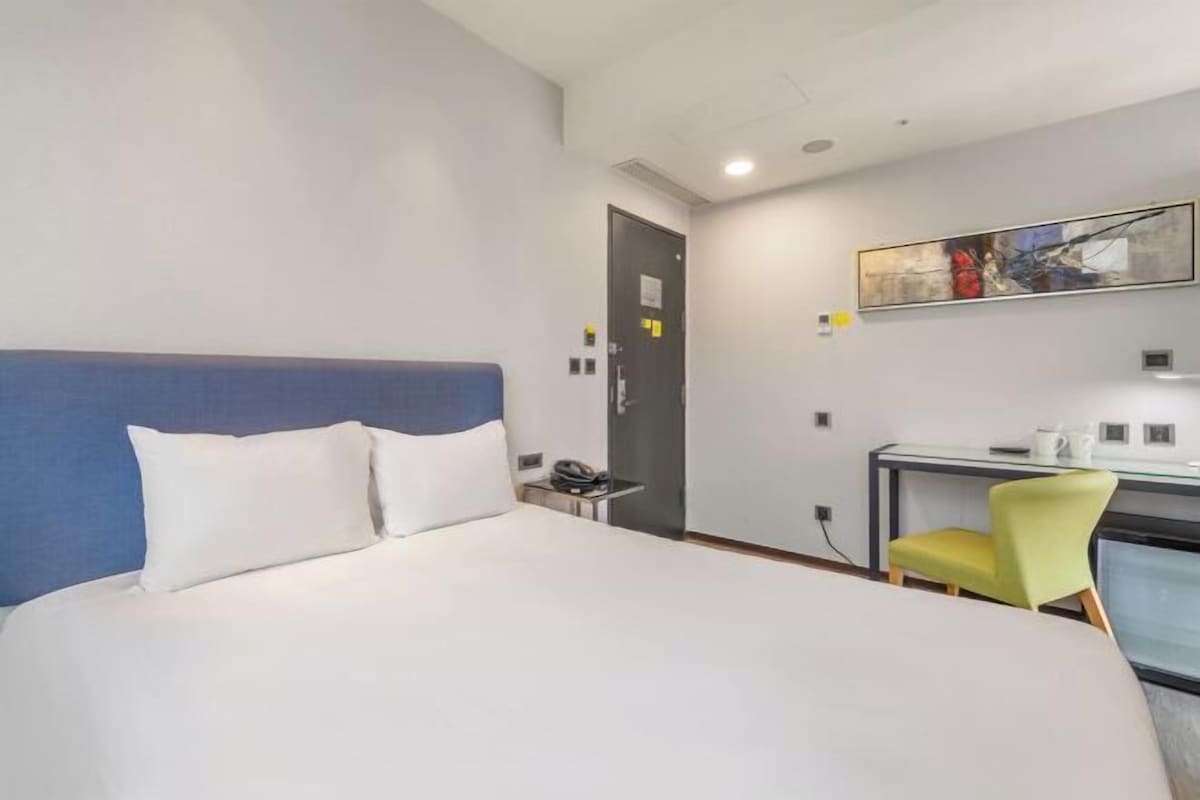Una habitación de hotel con una cama, un escritorio, una silla y un cuadro en la pared.