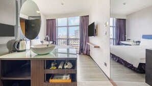 Una habitación de hotel moderna con un ventanal grande, una cama, un televisor, un lavabo y un espejo.