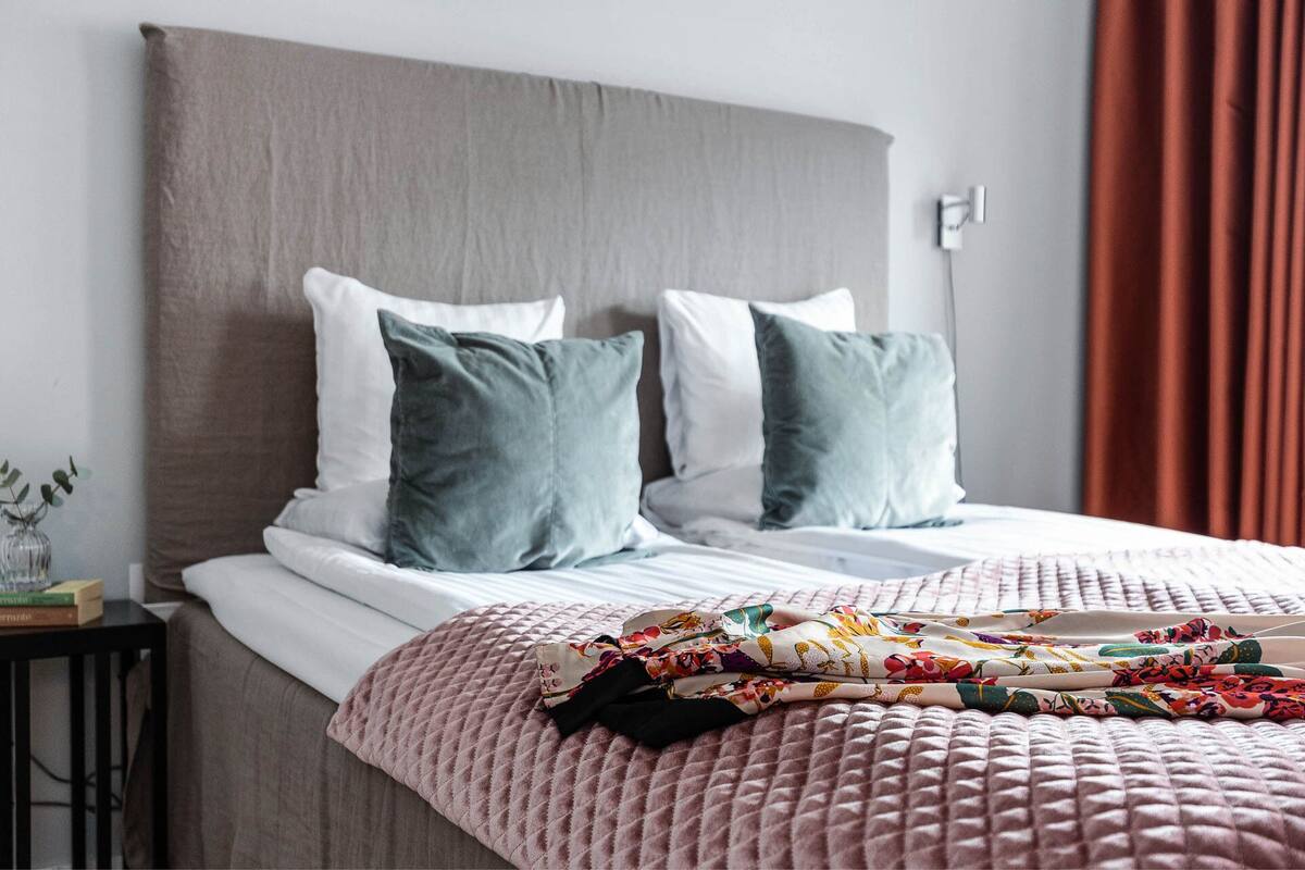 Een opgemaakt bed met een roze sprei, twee kussens en een kleurrijke deken.