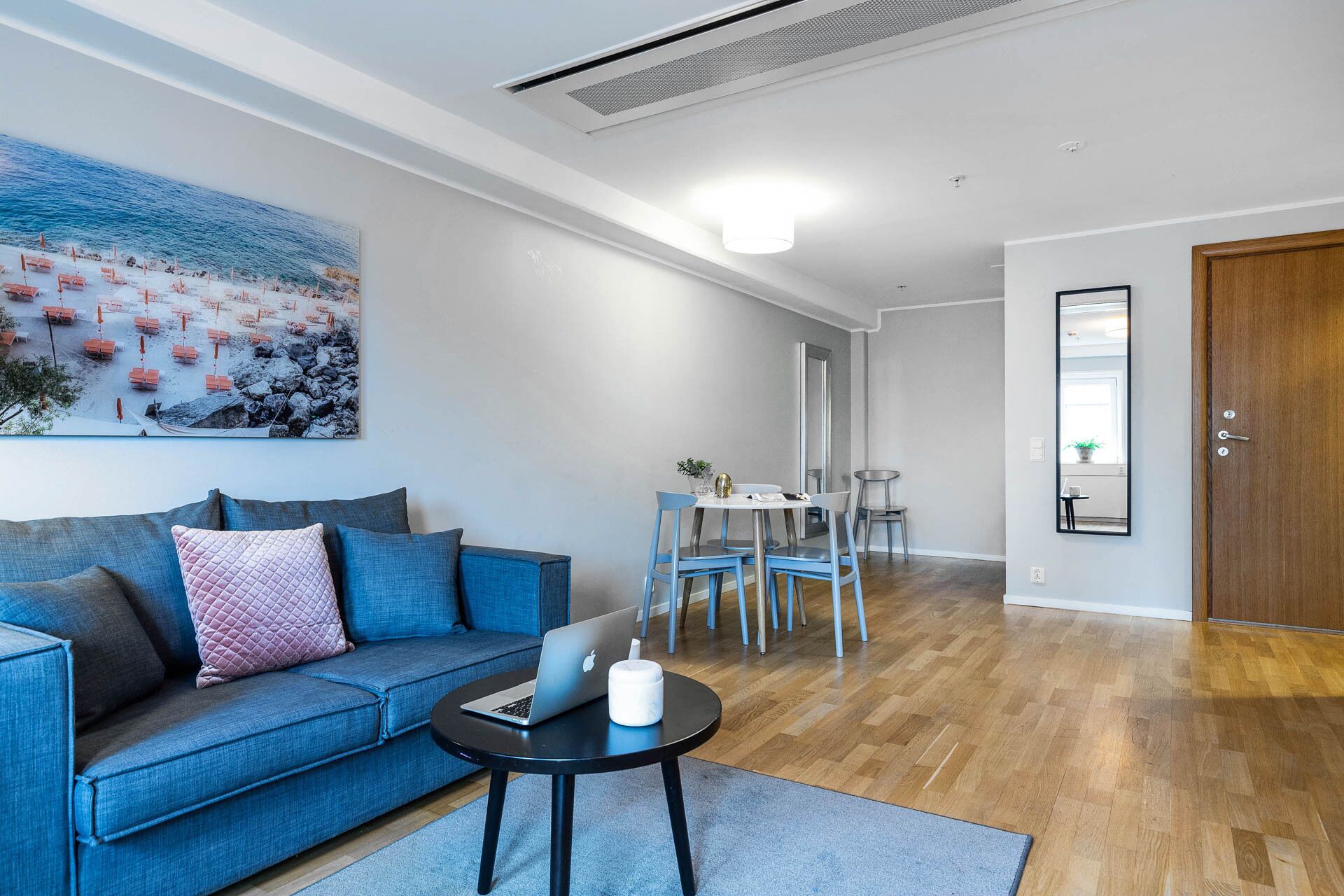 A modern living room with a blue sofa, a dining area with a table and chairs, and a wooden floor.