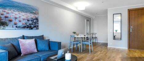 A modern living room with a blue sofa, a dining area with a table and chairs, and a wooden floor.