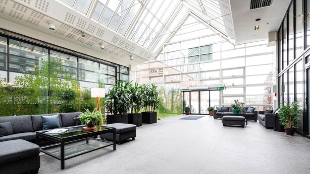 A spacious lobby with a high ceiling, large windows, and indoor plants. - Biz Apartment Gärdet (Stockholm)