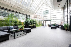 A spacious lobby with a high ceiling, large windows, and indoor plants. - Biz Apartment Gärdet (Stockholm)
