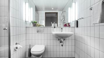 Un baño moderno con azulejos blancos, inodoro, lavabo y ducha.