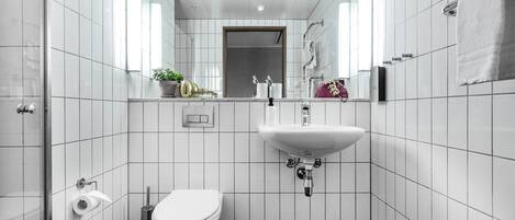 Ein modernes Badezimmer mit weißen Fliesen, einer Toilette, einem Waschbecken und einer Dusche.