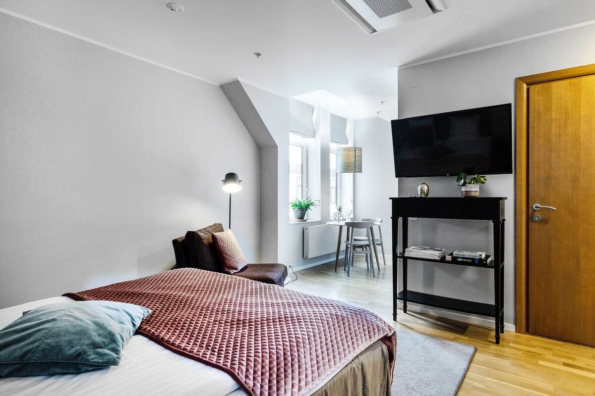 Een moderne slaapkamer met een bed, een bureau, een televisie en een houten deur.
