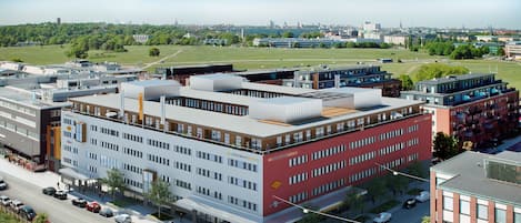 Un immeuble moderne à plusieurs étages, comprenant des espaces résidentiels et commerciaux, caractérisé par une façade rouge bien visible et un toit plat.