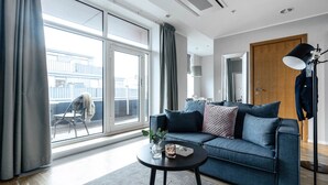 A modern living room with a sofa, a coffee table, and a large window. - Biz Apartment Gärdet (Stockholm)