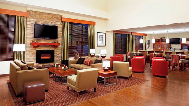 A hotel lobby with a fireplace, sofas, a television, and a dining area with red chairs. - Four Points by Sheraton Houston Hobby Airport (Houston)