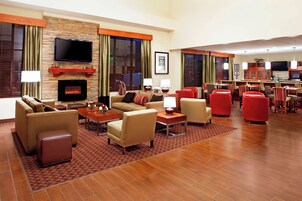 Un vestíbulo de hotel con chimenea, sofás, televisor y zona de comedor con sillas rojas.