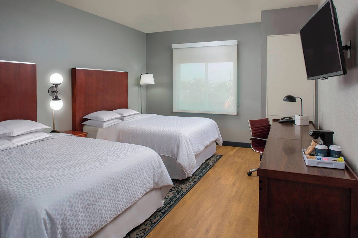A hotel room with two beds, a desk, a chair, a TV, and a window with a view.