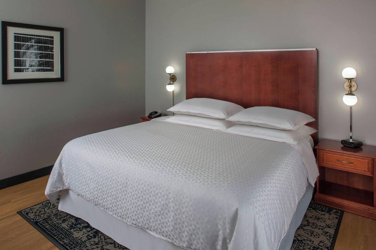 A neatly made bed with a patterned bedspread, two bedside lamps, a framed picture on the wall, and a wooden nightstand.