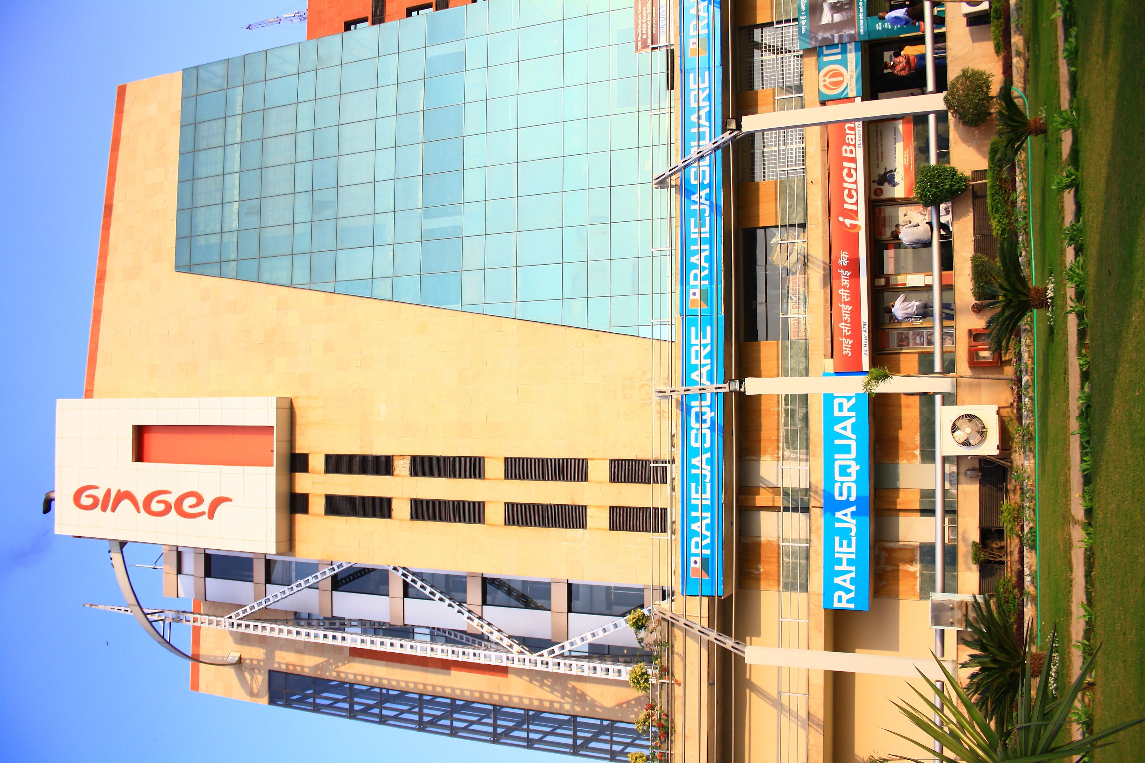 A multi-story building with a large glass facade, signage for 'RAHEJA SOLAR' and 'PRAJA SQUARE', and a 'Ginger' sign on the left.