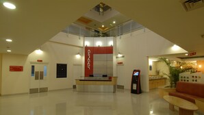 A modern hotel lobby with a reception desk, a seating area, and a staircase leading to an upper level. - Ginger Manesar (Gurugram)