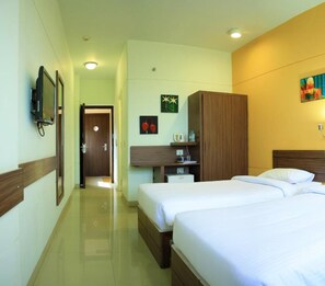 A hotel room with two beds, a wooden wardrobe, a desk with a chair, a small table with a kettle, and a wall-mounted TV. - Ginger Manesar (Gurugram)