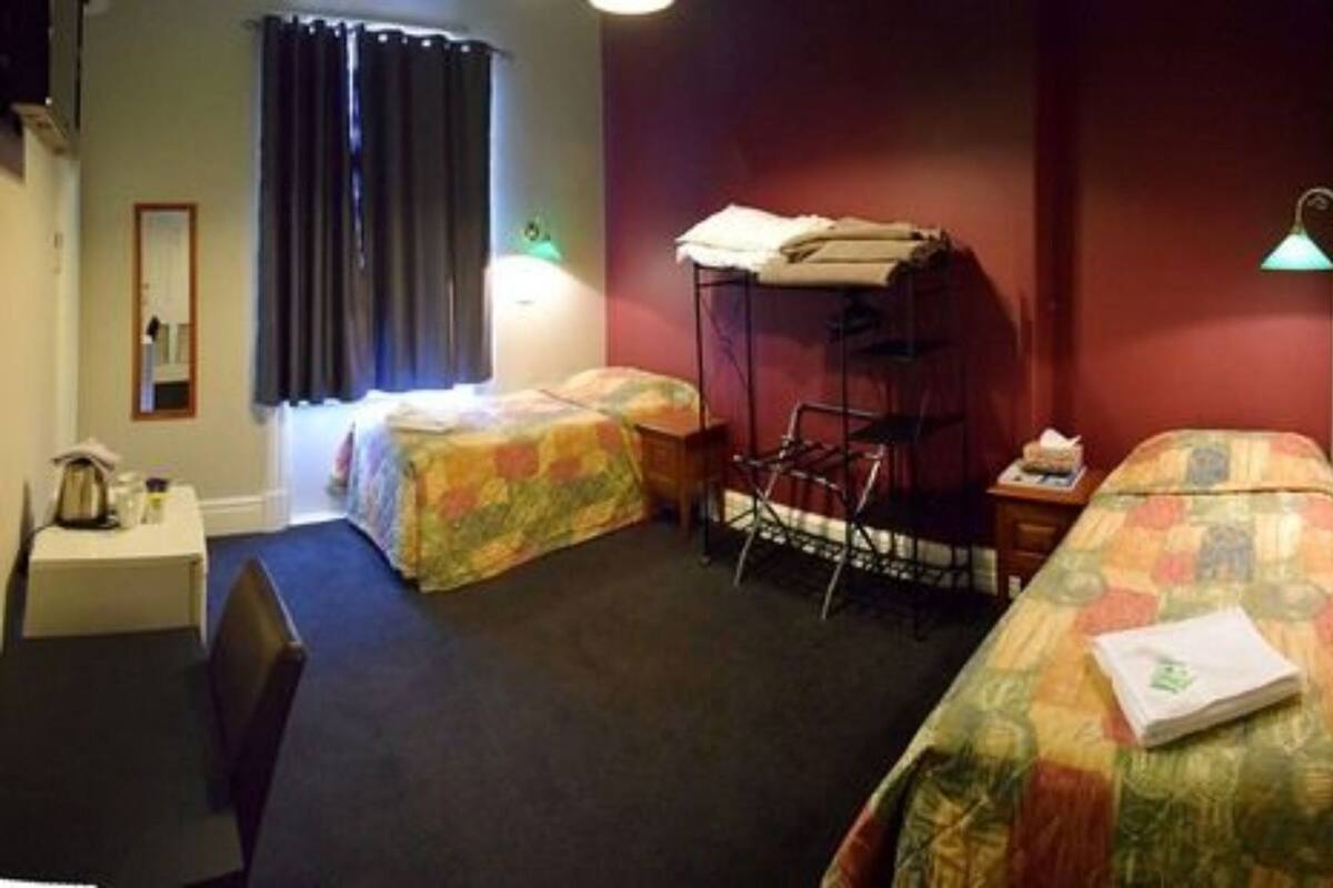 Une chambre d’hôtel avec deux lits, un bureau, une chaise, une petite table et une fenêtre avec des rideaux.