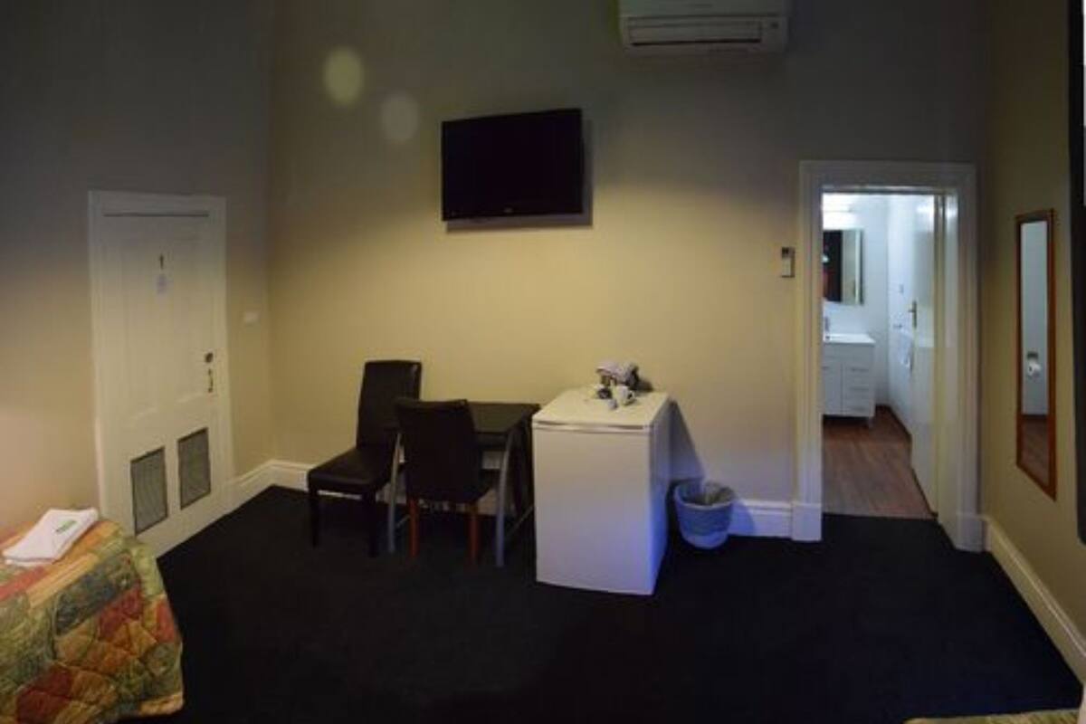 Une petite pièce faiblement éclairée, avec un bureau, deux chaises, un téléviseur et une poubelle.