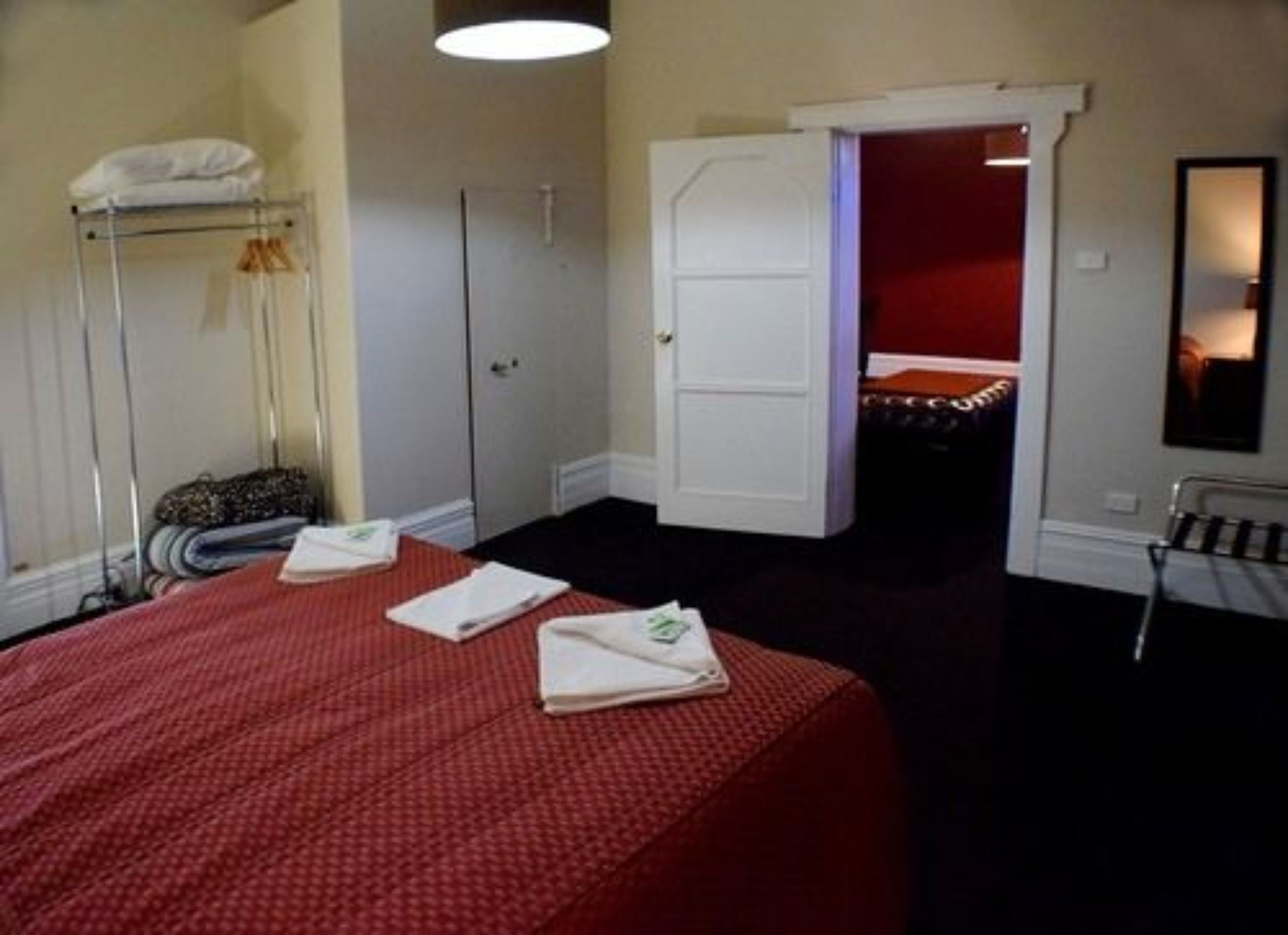 Een hotelkamer met een opgemaakt bed, een kledingkast, een spiegel en een deur naar een andere kamer.