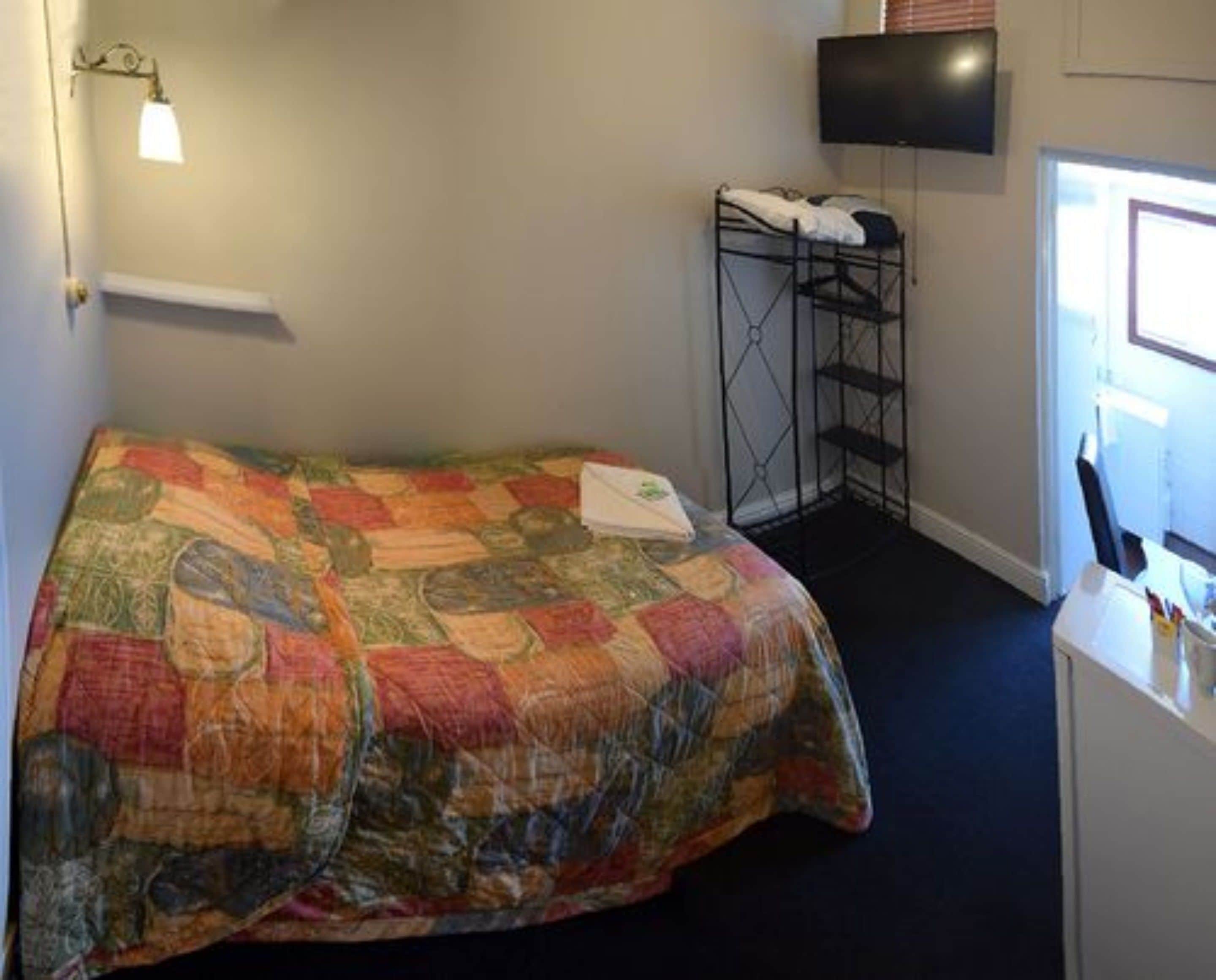 A room with a bed, a TV mounted on the wall, and a small desk with a chair.