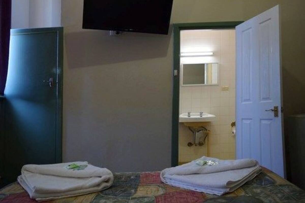 Une chambre d’hôtel avec un lit, un téléviseur fixé au mur, un appareil de climatisation, une porte et une salle de bain visible à travers une porte ouverte.