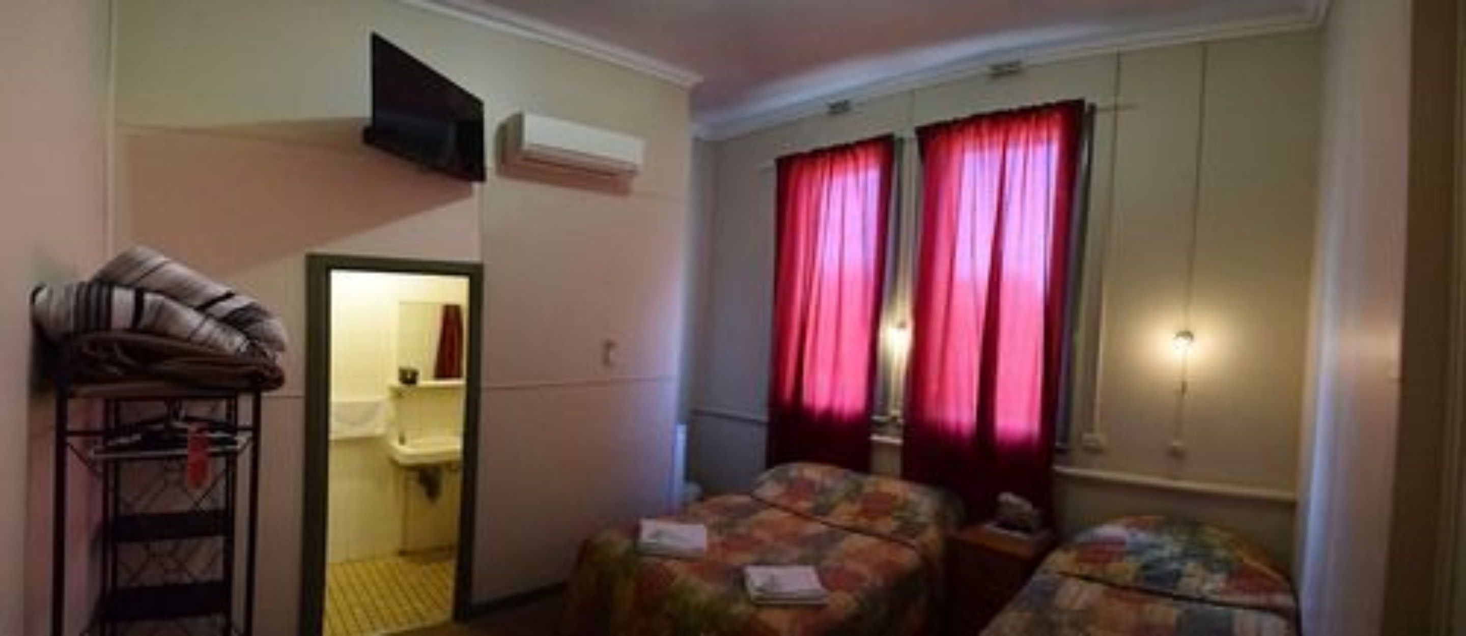 Habitación de hotel con dos camas, un armario, baño con lavamanos y un televisor montado en la pared.