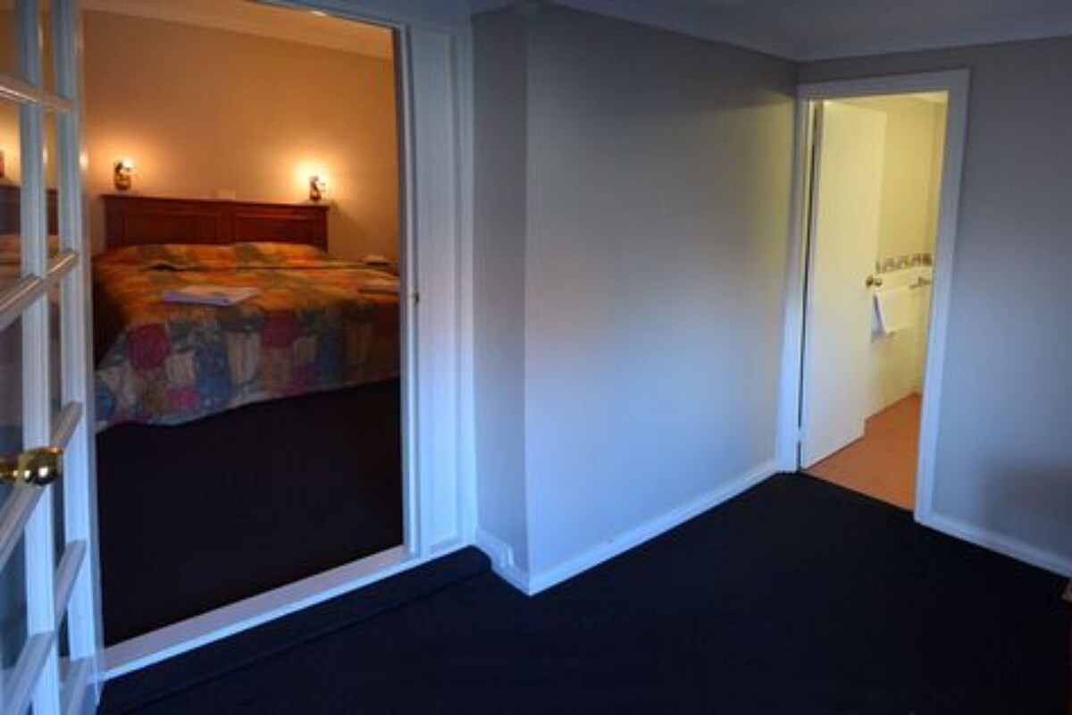 A bedroom with a bed, a door leading to another room, and a carpeted floor.