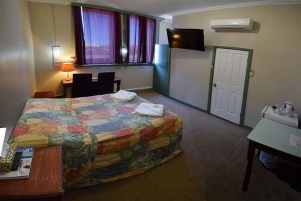 Ein Hotelzimmer mit Bett, Schreibtisch, Sessel, Wandfernseher und einer Tür.