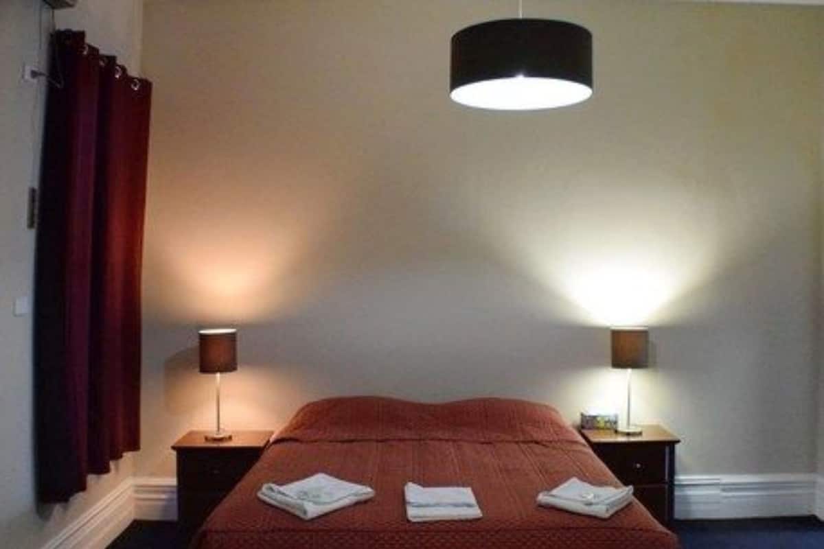 Un lit bien fait, recouvert d’une couverture rouge, avec deux lampes de chevet.