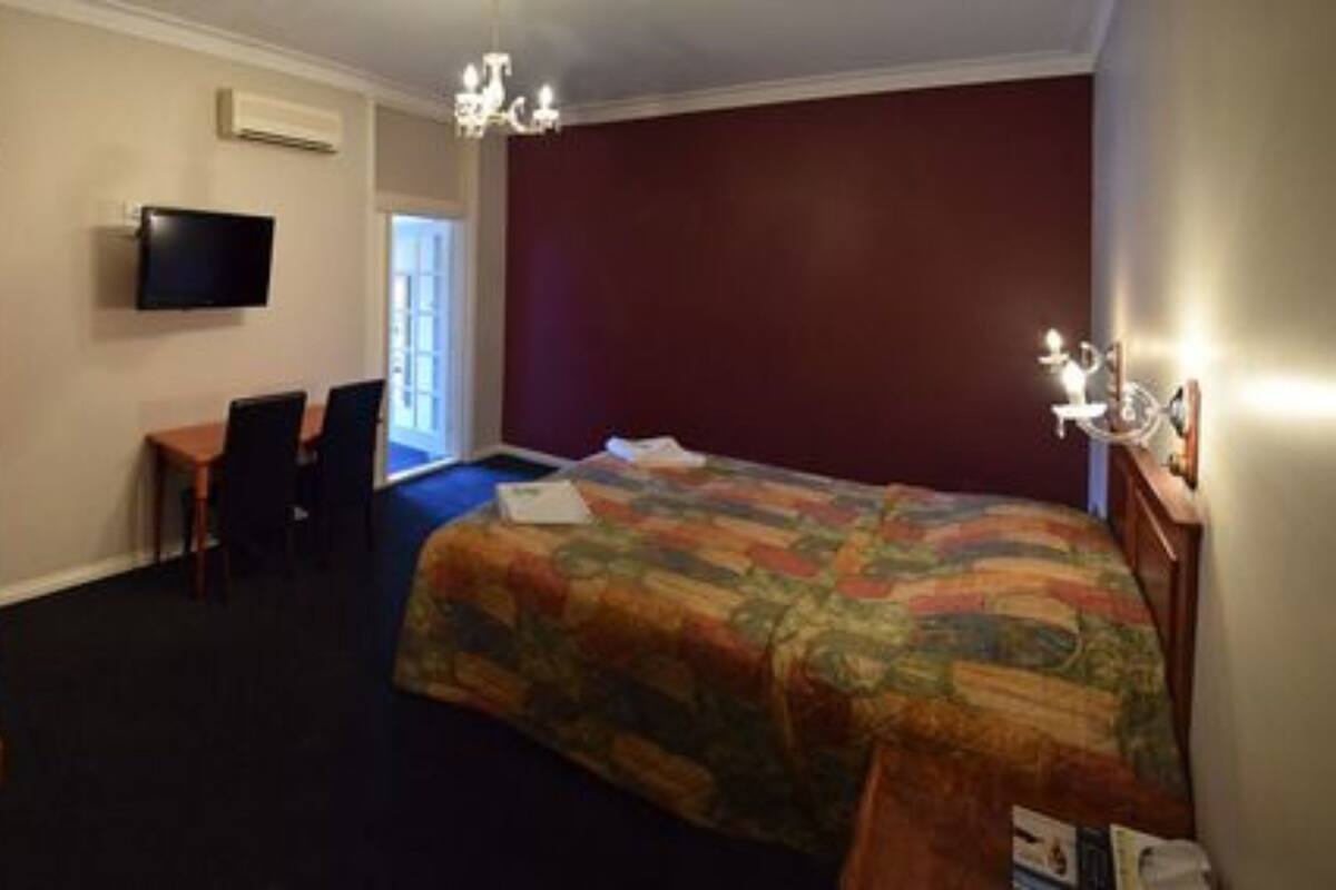 Une chambre à coucher comprenant un lit, un bureau, deux chaises, un téléviseur et un lustre.