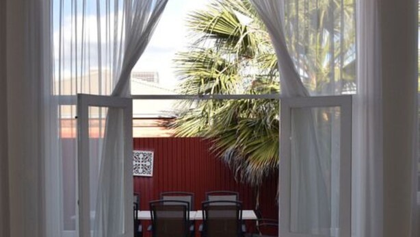 An open doorway leading to an outdoor patio with a red wall, a palm tree, and a table with chairs. - Palace Hotel Kalgoorlie (Kalgoorlie)