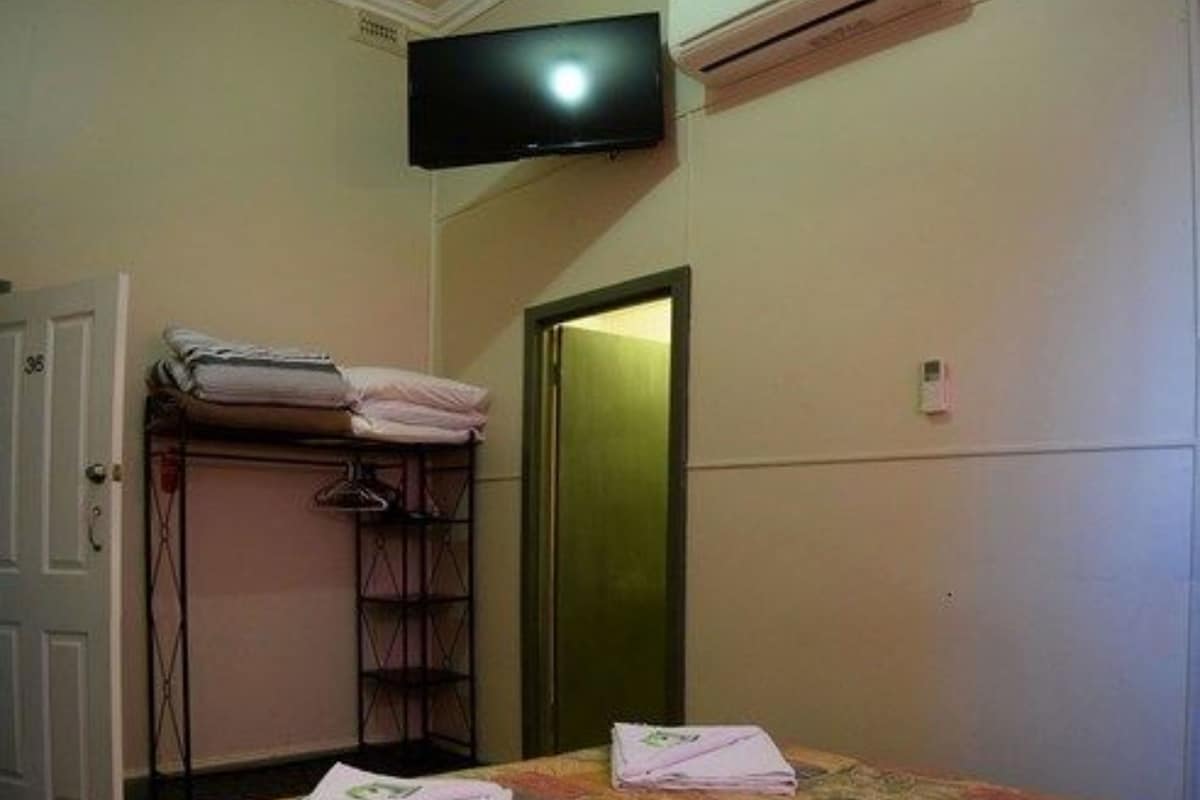 Ein kleiner, schlichter Raum mit einem Bett, einem an der Wand montierten Fernseher und einer Klimaanlage.