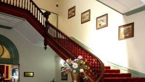 A grand staircase with red carpeted steps, a wooden railing, and a floral arrangement at the top. - Palace Hotel Kalgoorlie (Kalgoorlie)