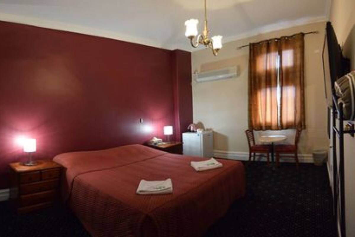 Une chambre d’hôtel avec un grand lit, deux tables de chevet, un bureau avec une chaise, un lustre et une fenêtre avec des rideaux.