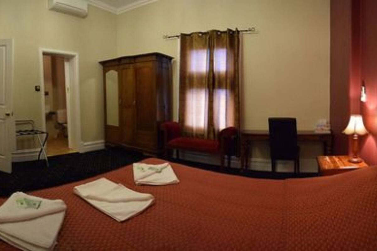 Une chambre d’hôtel comprenant un lit, un bureau, une chaise, une armoire et une porte donnant sur une autre pièce.