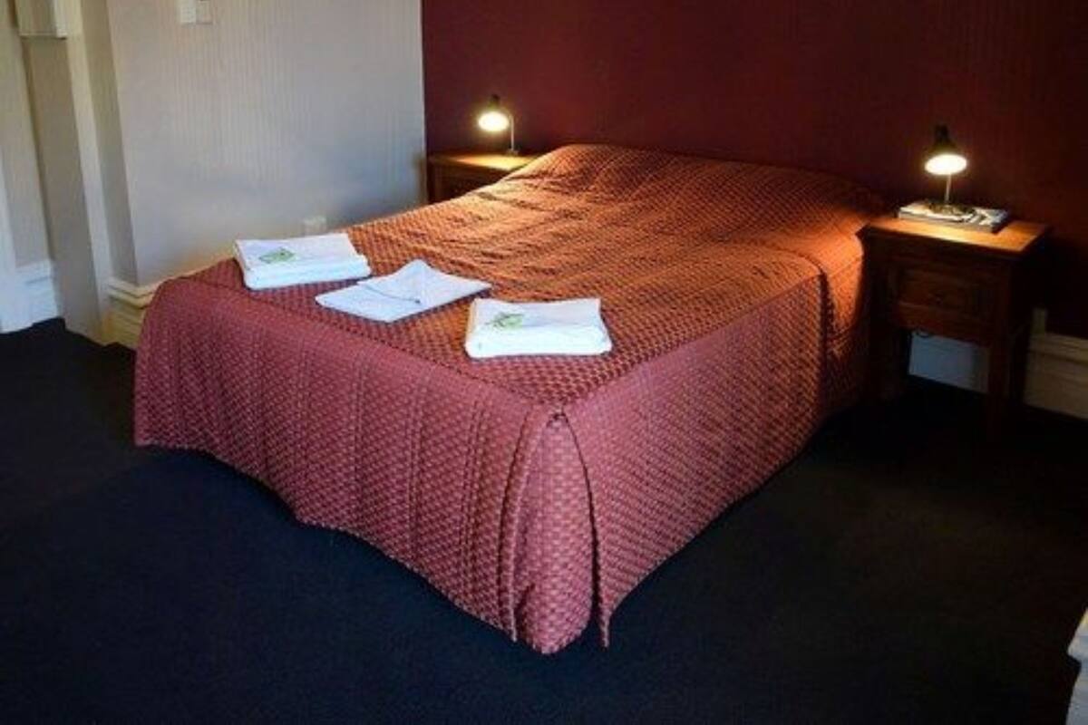 Un lit bien fait, avec une couverture rouge et deux serviettes blanches, deux lampes de chevet et une table de chevet en bois.