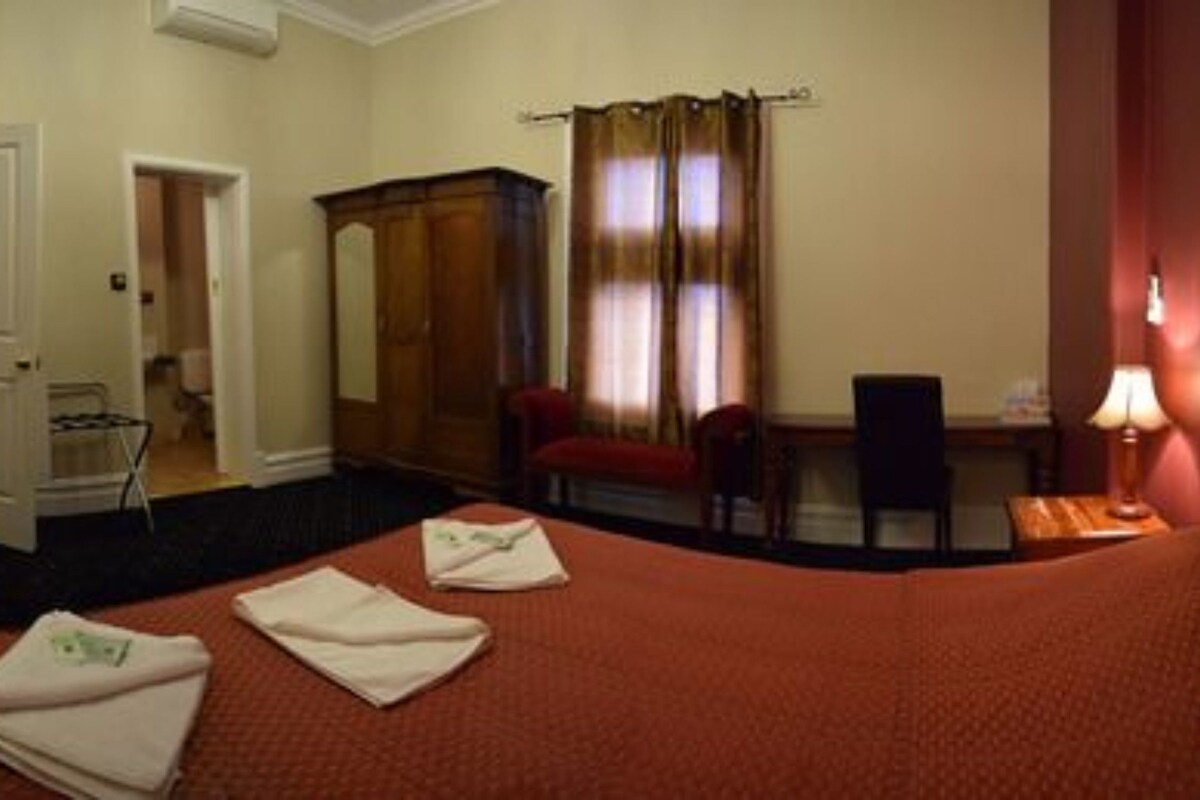 Ein Hotelzimmer mit Bett, Schreibtisch, Stuhl, Kleiderschrank und einem durchgegangenen Tür erkennbaren Badezimmer.