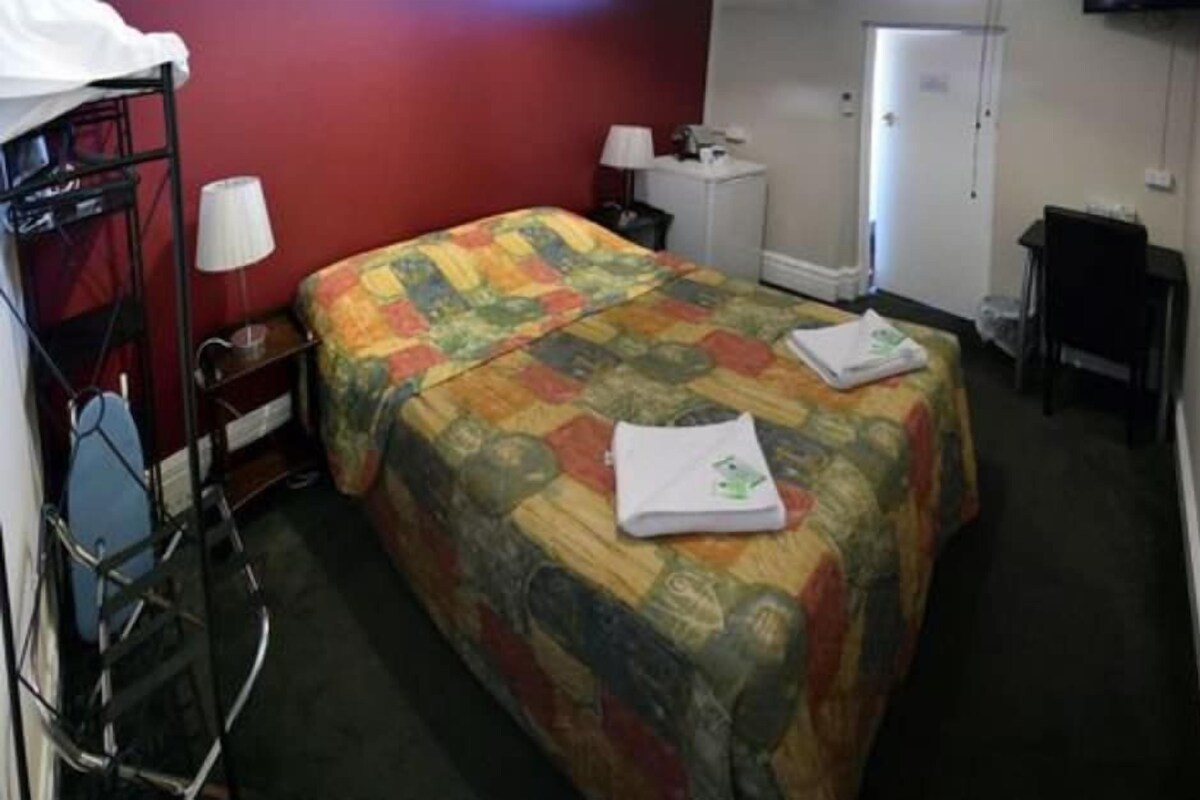 Ein Hotelzimmer mit Bett, Schreibtisch, Stuhl, Lampe und Kleiderschrank.