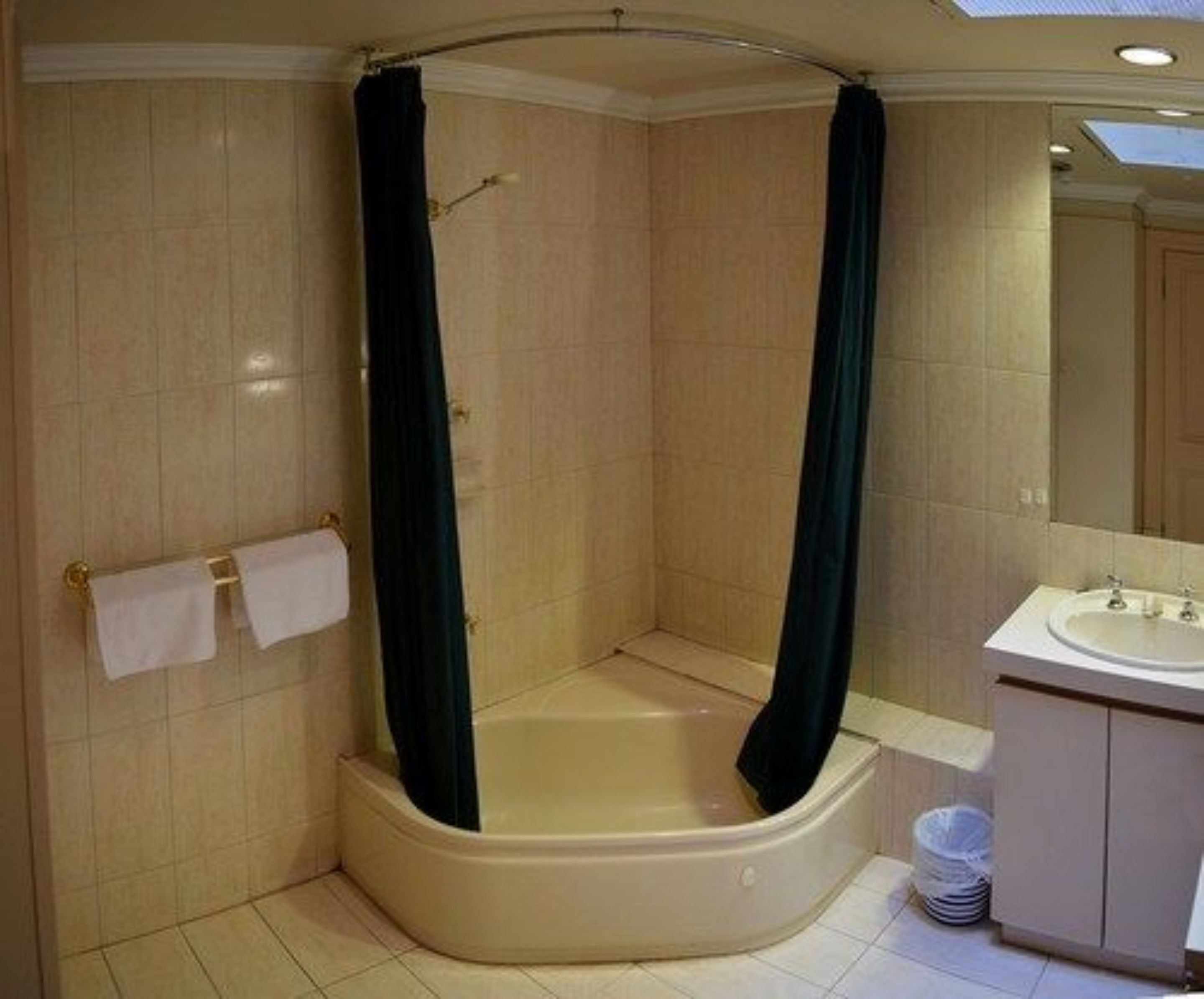 Una ducha a pie con bañera, un perchero con dos toallas blancas, un lavamanos y un espejo.