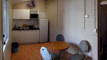 A compact kitchen with white cabinets, a microwave, and a small refrigerator. There is a dining table with two chairs and a potted plant on the counter.