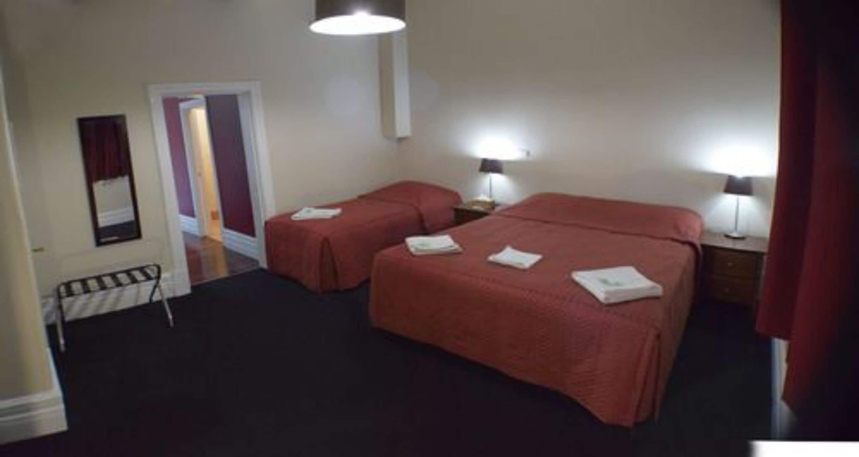 A hotel room with two beds, a small desk, a chair, and a door leading to another room.