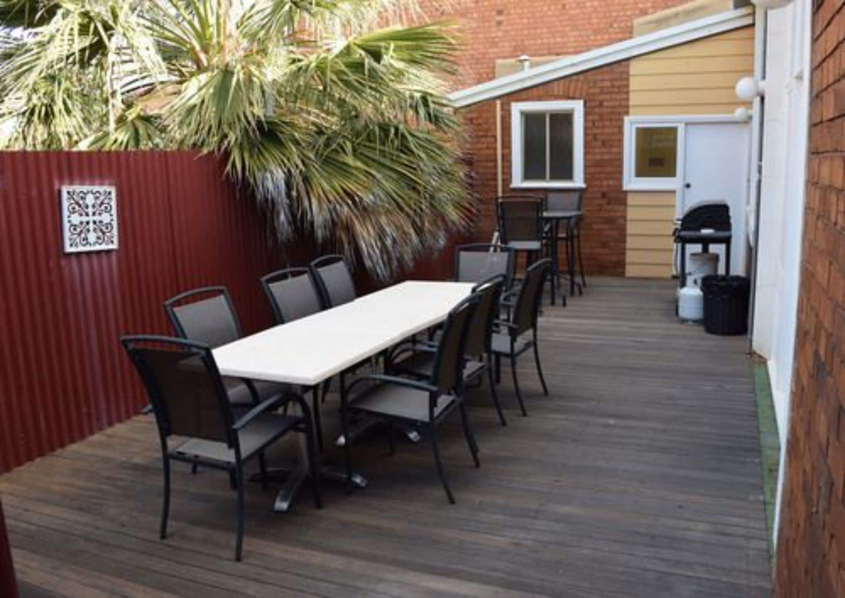 A patio with a long table and chairs, a red fence, and a door in the background.