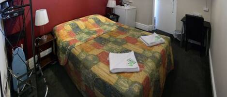 A hotel room with a bed, a desk, a chair, a lamp, and a door.