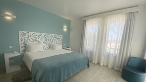 Une chambre à coucher moderne, avec un lit, une table de chevet, une chaise et une grande fenêtre ornée de rideaux légers.